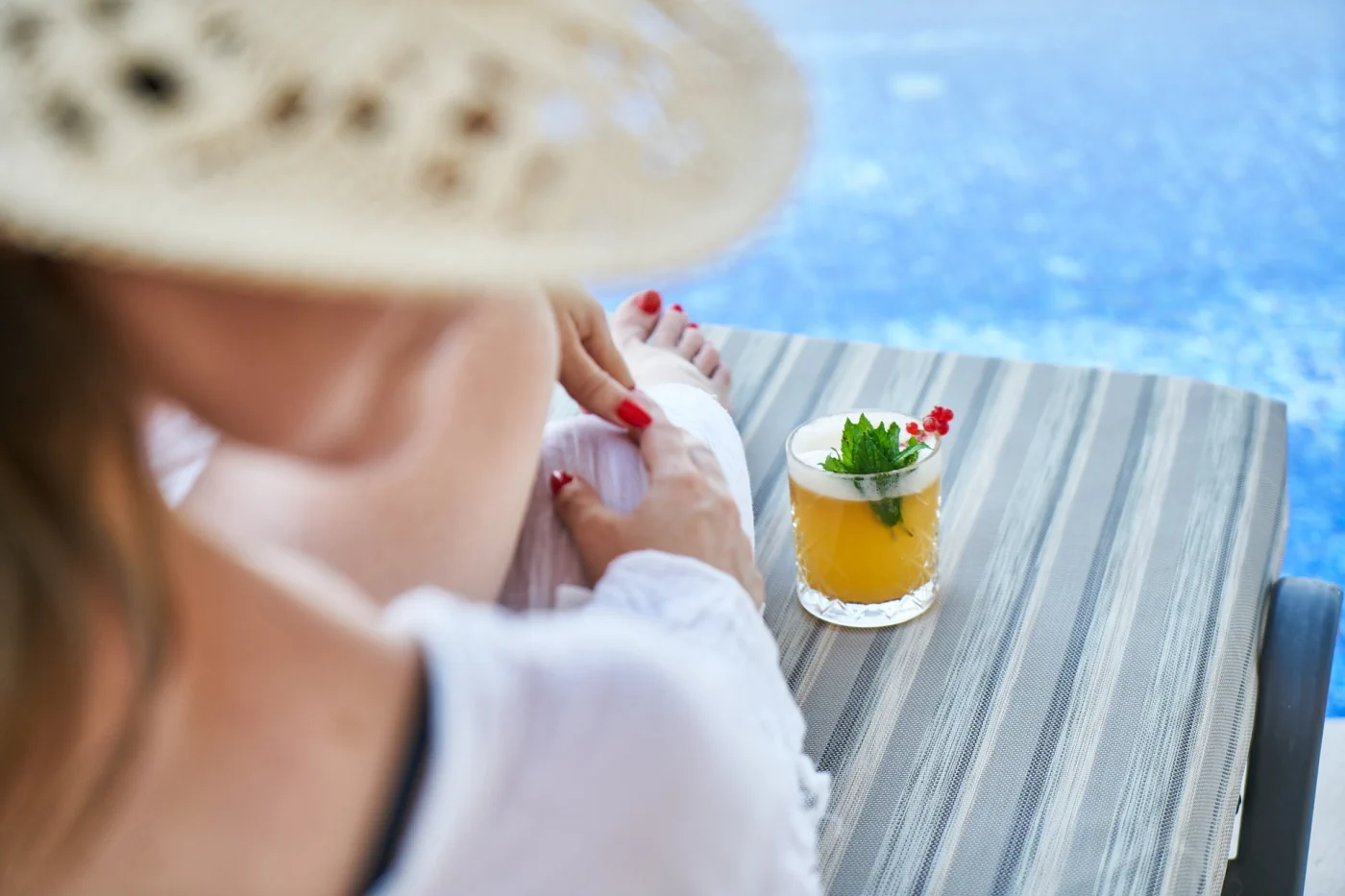 spf solskyddsfaktor - kvinna vid vattnet i solen med drink och hatt